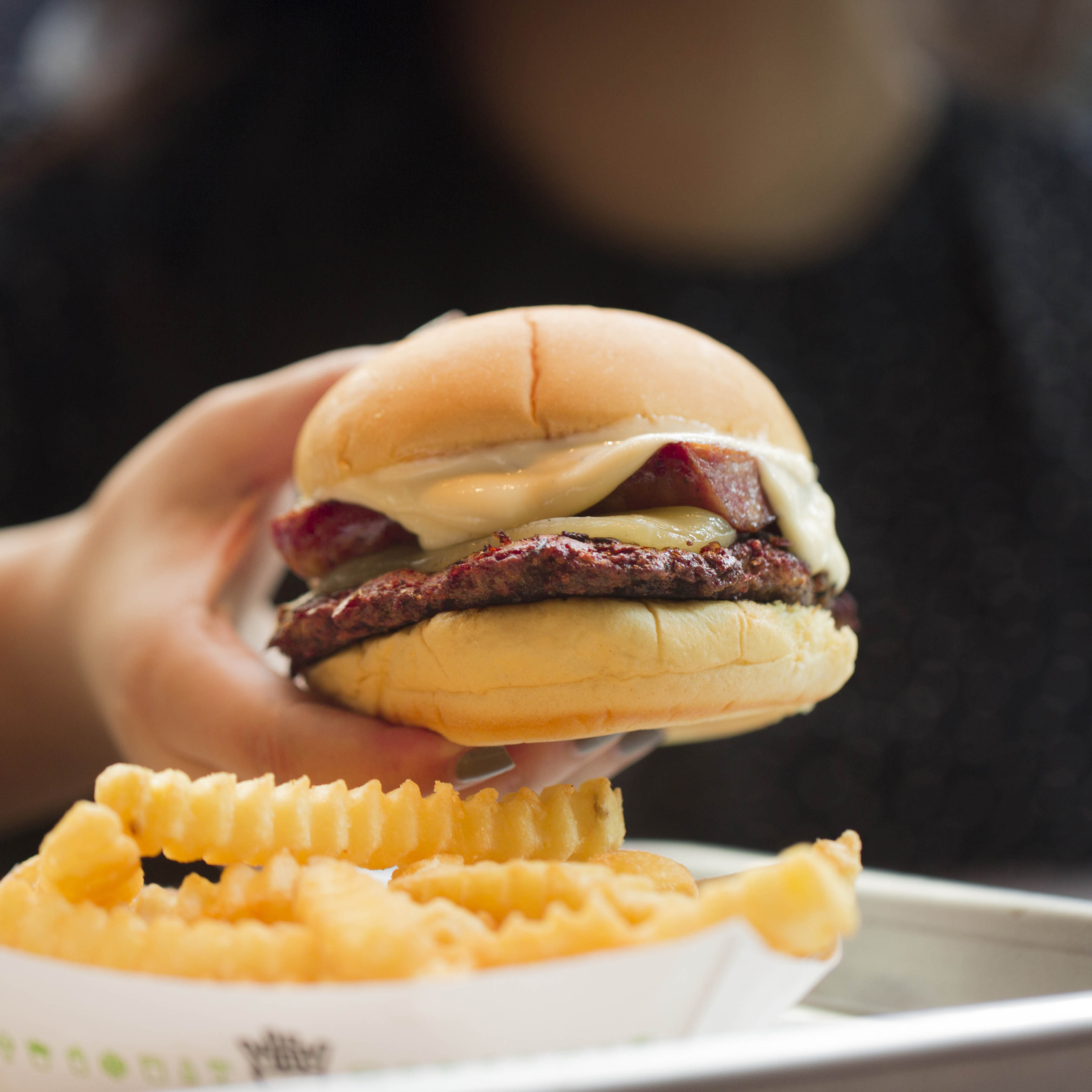 PQM BratBurger being held in a hand with fries in the foreground