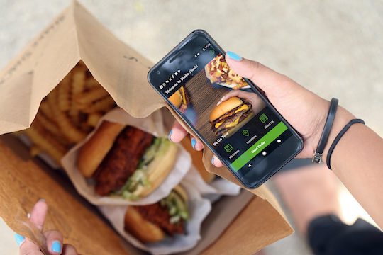 smartphone held in hand over shake shack burger and fries