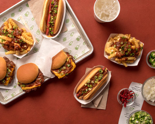 Chili Fries, Chili Burgers, Chili Dogs and a soda displayed on a table