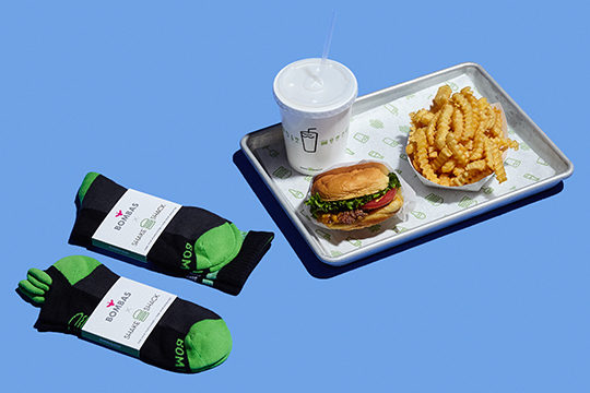 Shake Shack drink, burger, and fries on a tray next to Bombas socks