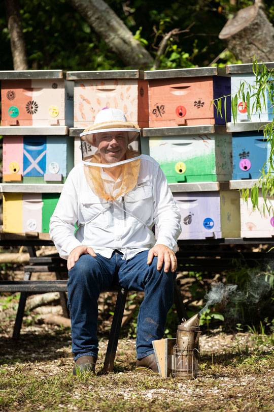 Beekeeper Damon Roy sitting in apiary