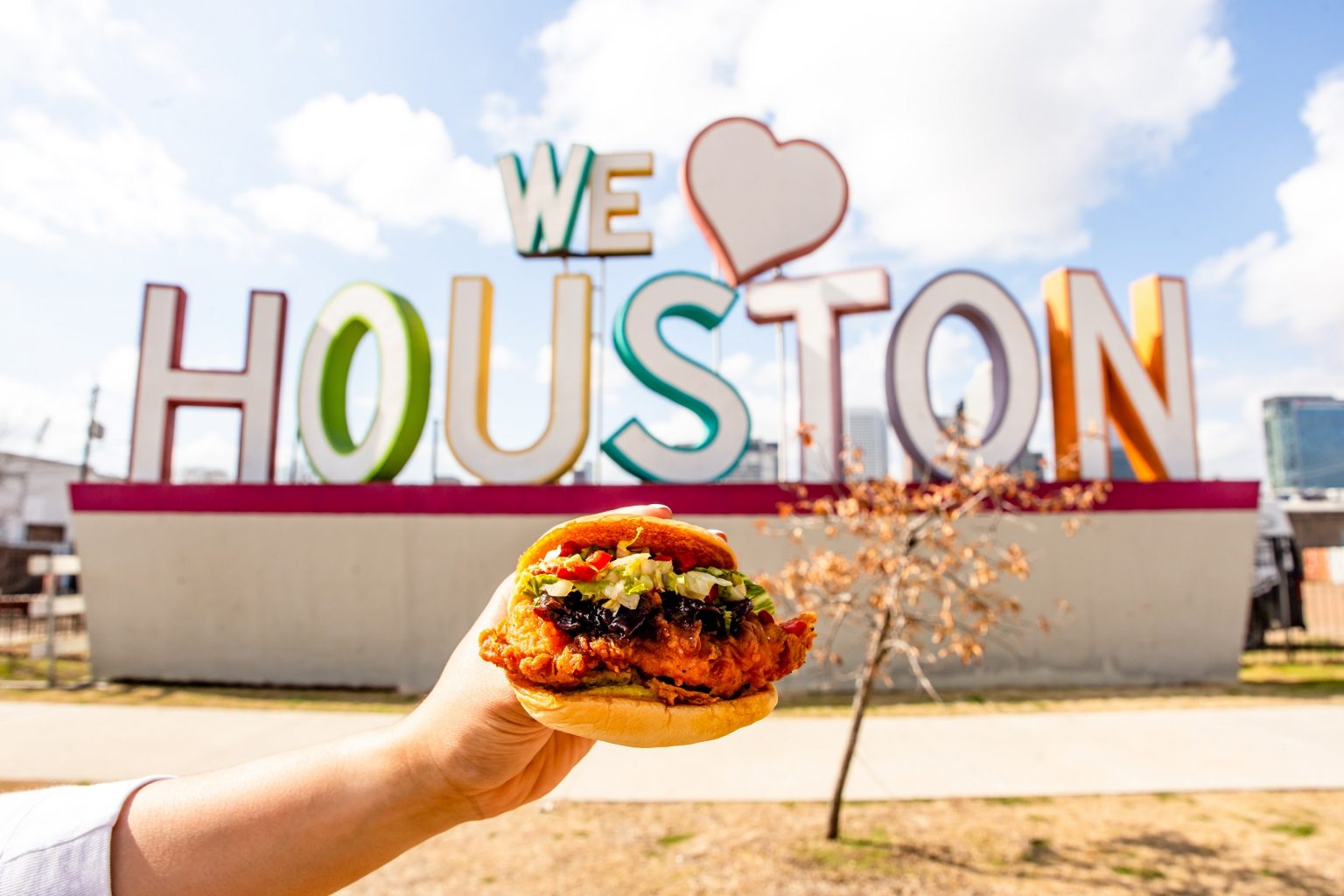 hand holding sandwich in front of We Heart Houston sign