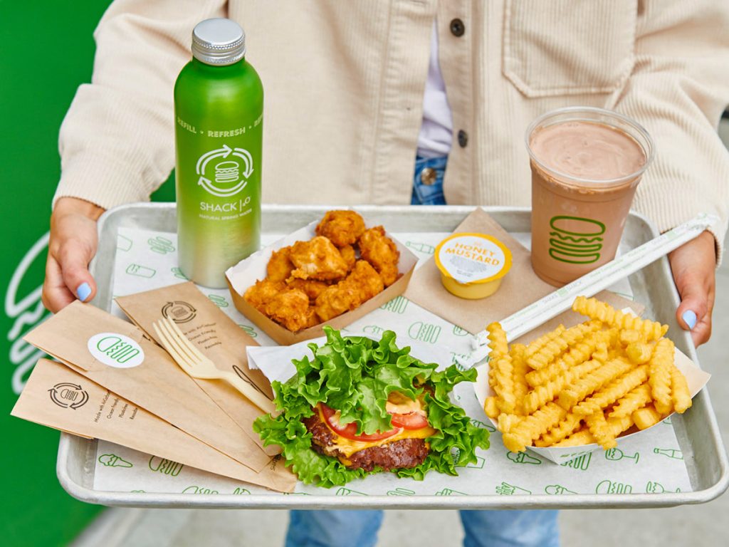 Hands holding tray of various Shake Shack food and drinks