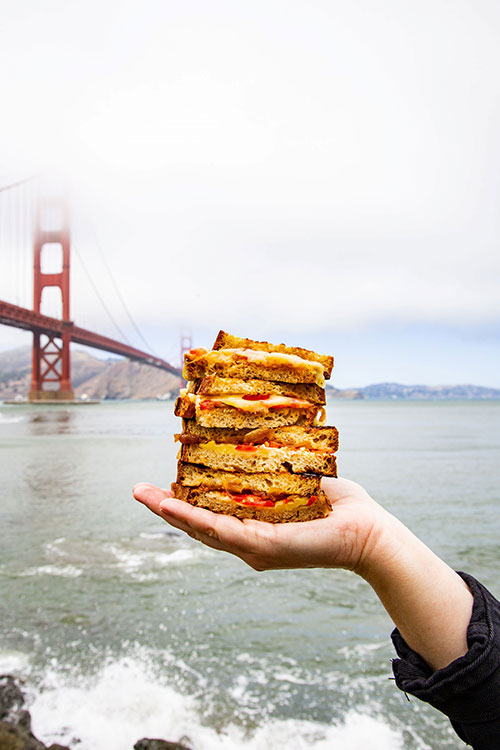 Hand holding a stack of grilled cheese sandwiches with the Golden Gate bridge in the background