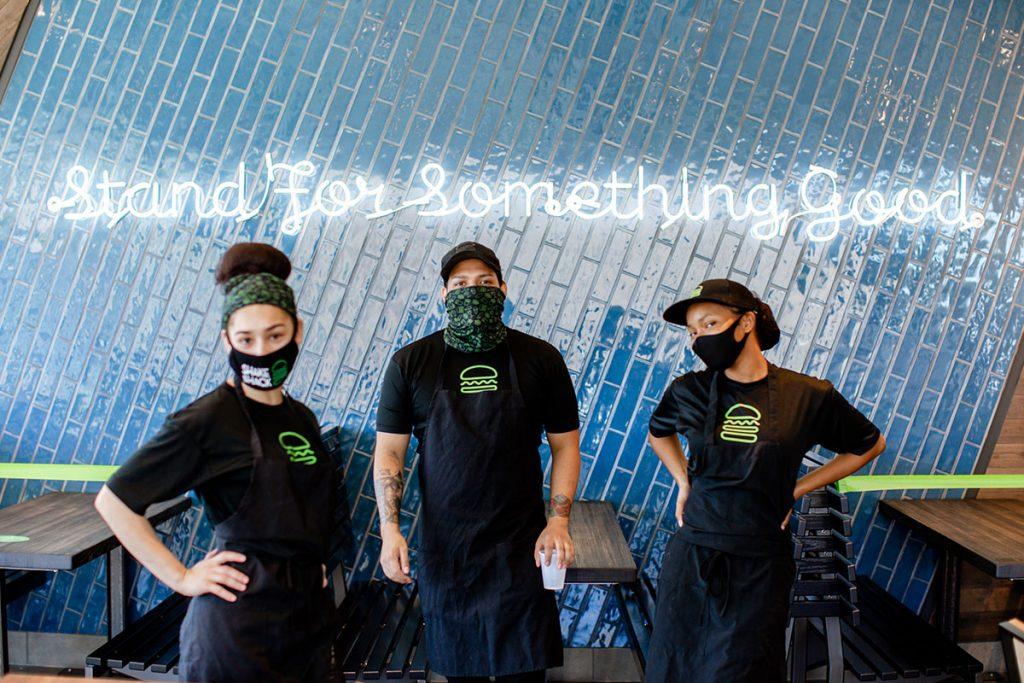 Shake Shack employees posing by a wall that reads Stand for Something Good
