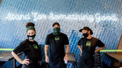Shake Shack employees posing by a wall that reads Stand for Something Good