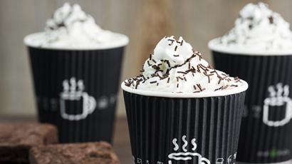 three shakes sitting on a counter top with whipped cream and dark sprinkles. There are two brownies sitting next to one of the shakes.