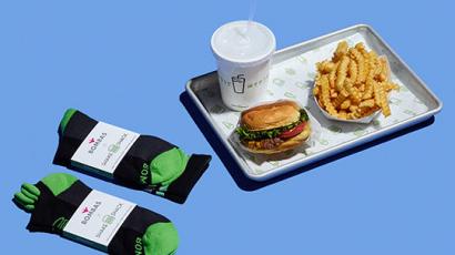 burger, fries and drink sitting on a tray. There are two pair of Bombas branded, black and white socks sitting next to the tray