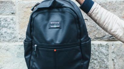 hand holding a black backpack in front of a stone wall