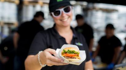 shake shack employee wearing sun glasses, handing a burger to the camera