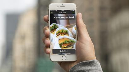 hand holding a phone with the shake shack app on it. Behind it is a blurred out city street.